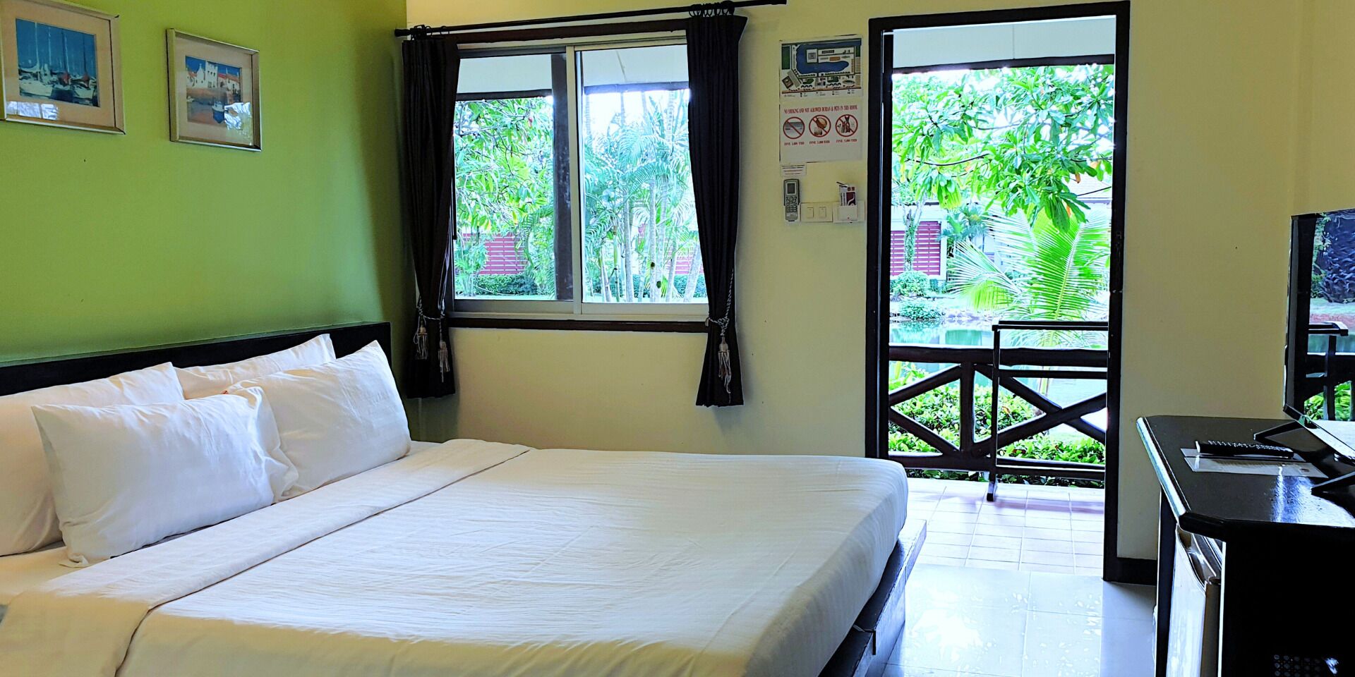 A hotel room with a bed, a desk, and a view of greenery outside.