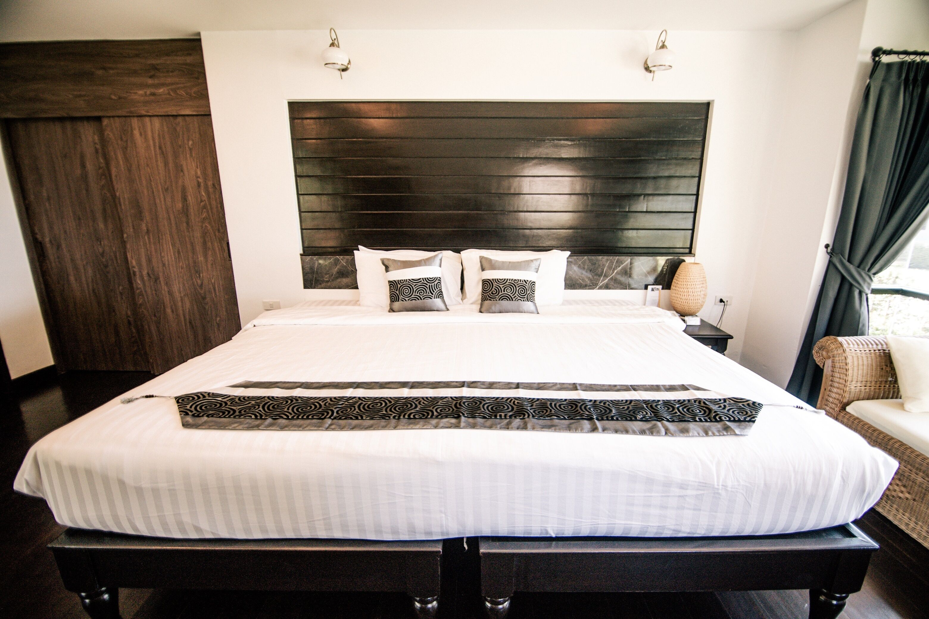 A neatly made bed with a patterned bedspread, a dark headboard, and a nightstand with a lamp.