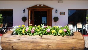 A wooden log planter filled with colorful flowers in front of a building with a wooden door and two lanterns on either side. - Nord Hotel (Cortina d'Ampezzo)