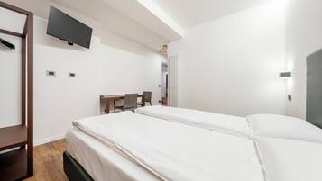 A hotel room with a bed, a desk, a chair, a TV mounted on the wall, and a radiator.