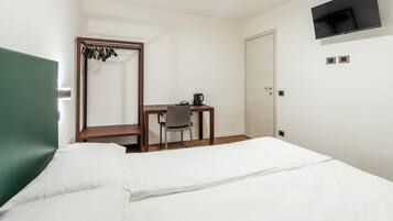 A hotel room with a bed, a desk with a chair, a coat rack, a television, and a door.