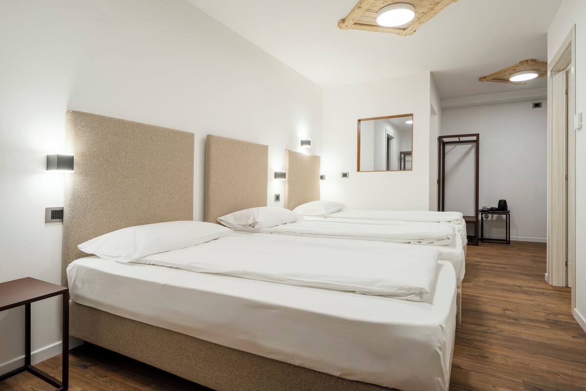A hotel room with two beds, a wooden floor, a small table, and a mirror on the wall.