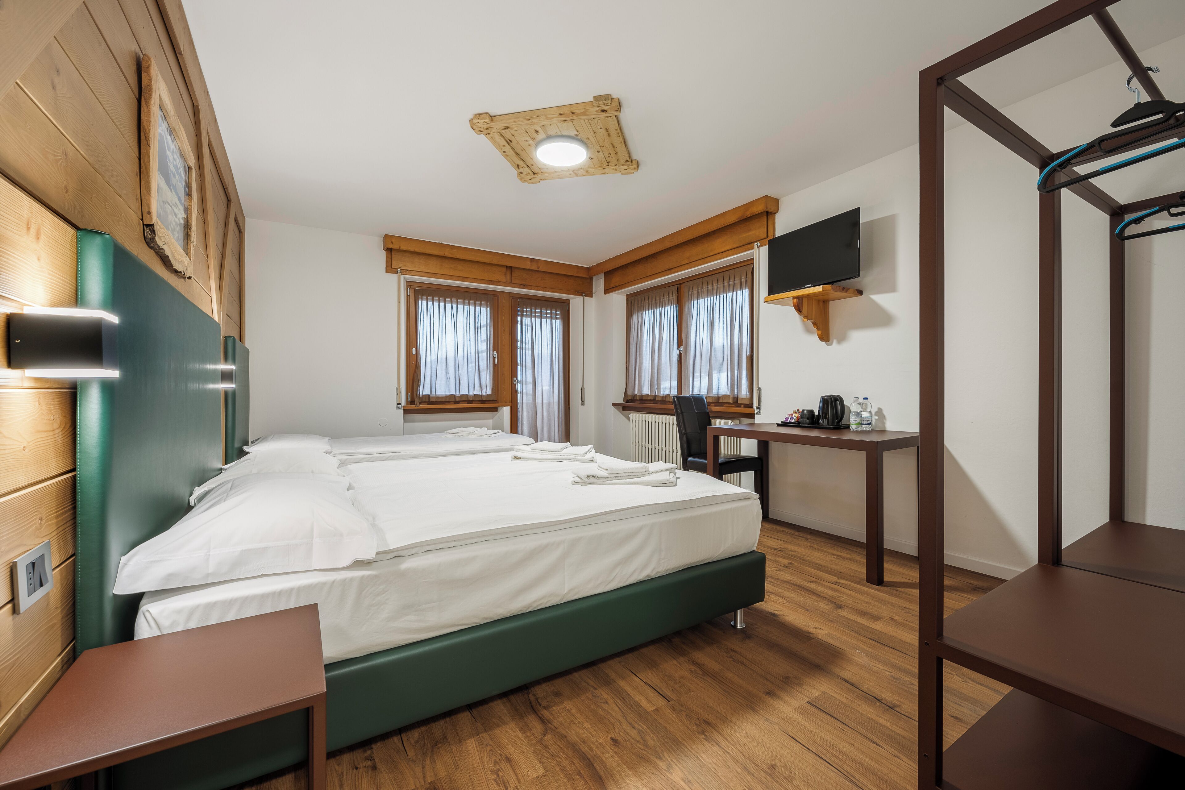 A hotel room with a bed, a desk, a chair, a TV, and a window with curtains.