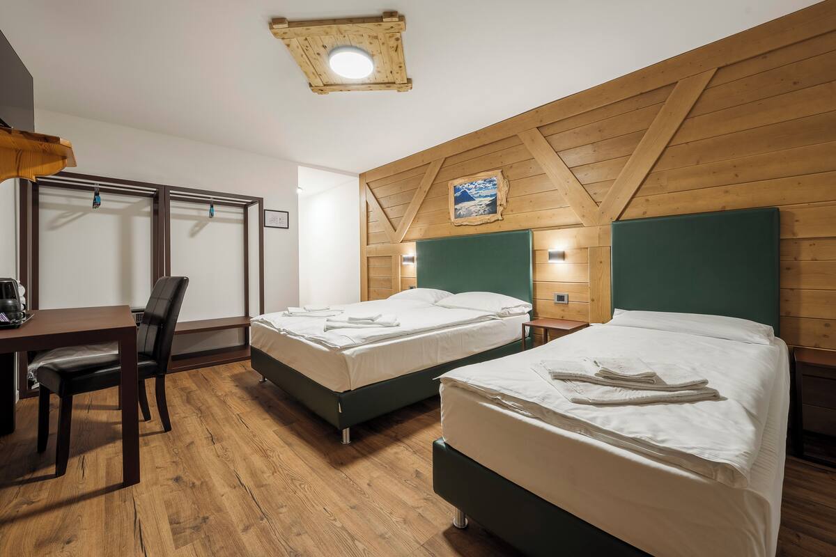 A hotel room with two beds, a desk, a chair, and wooden walls.