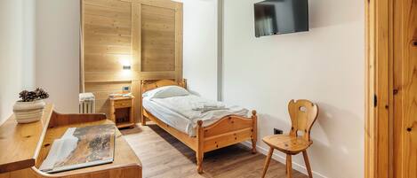 Un dormitorio con una cama de madera, un televisor montado en la pared, una silla de madera y un escritorio con una revista.