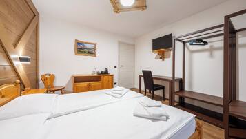 A bedroom with a bed, wooden headboard, a desk with a chair, a TV mounted on the wall, and a wooden wardrobe.