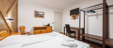 A bedroom with a bed, wooden headboard, a desk with a chair, a TV mounted on the wall, and a wooden wardrobe.