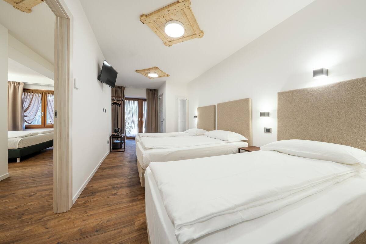 A hotel room with two beds, a television, a ceiling fan, and a wooden floor.