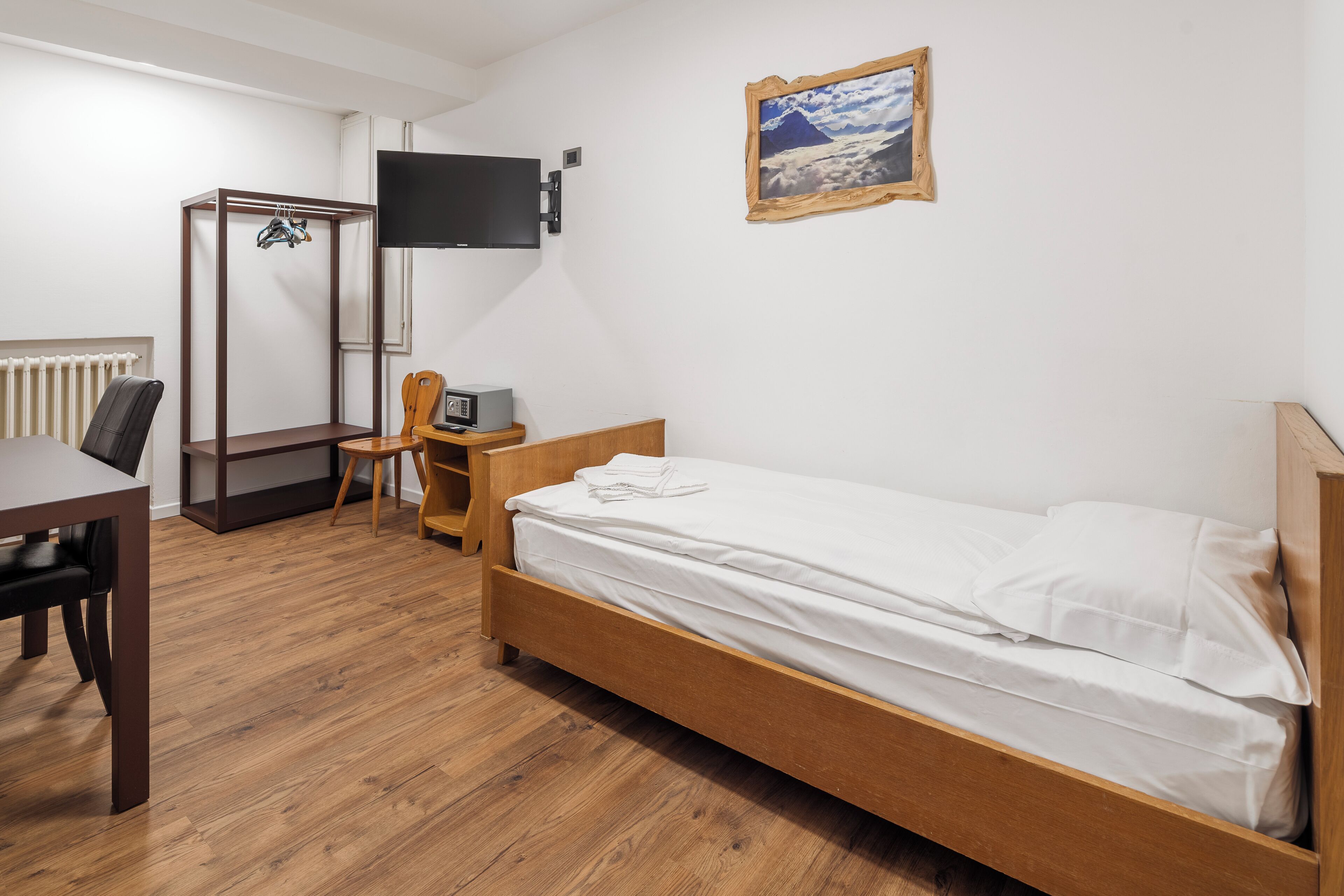 Una camera da letto con un letto di legno, una scrivania, una sedia, una TV e un termosifone.