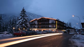 A hotel with a snow-covered landscape, a road with light trails, and parked cars.