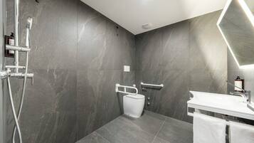 A modern bathroom with a shower, toilet, and sink, featuring grey marble walls and a white vanity.