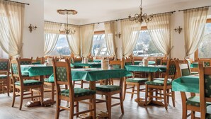 A dining area with wooden chairs and tables, large windows with curtains, and chandeliers. - Nord Hotel (Cortina d'Ampezzo)