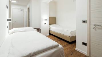 Una camera d'albergo con un letto grande, un letto più piccolo, un comodino, un armadio e una porta con maniglia.