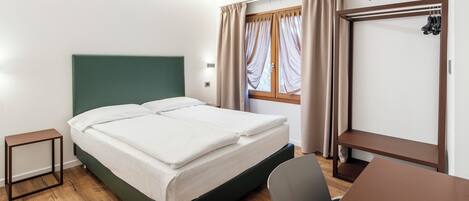 Habitació d'hotel ben ordenada, amb llit, escriptori, cadira i televisió penjada a la paret.