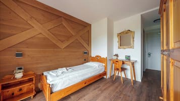 Un dormitorio con una cama de madera, una mesita de noche de madera, un escritorio con silla y un espejo en la pared.