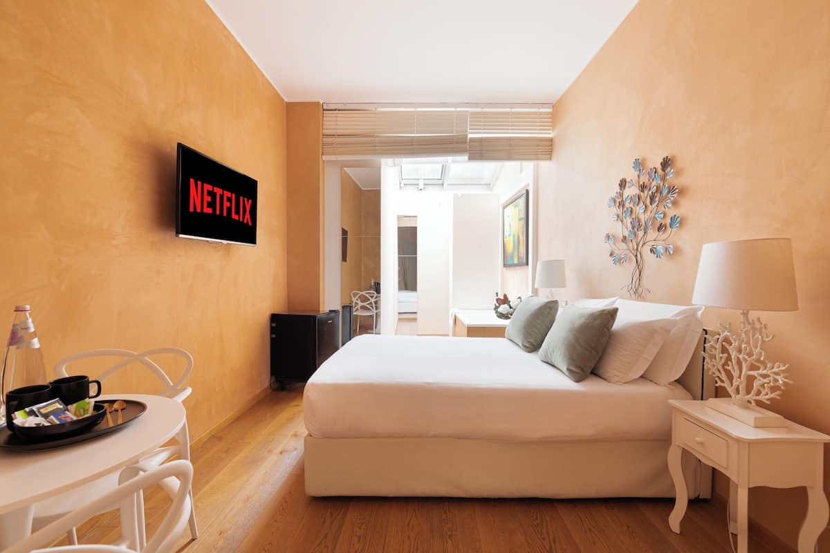 A hotel room with a bed, a TV displaying 'NETFLIX', a small table with a tray, and a lamp.
