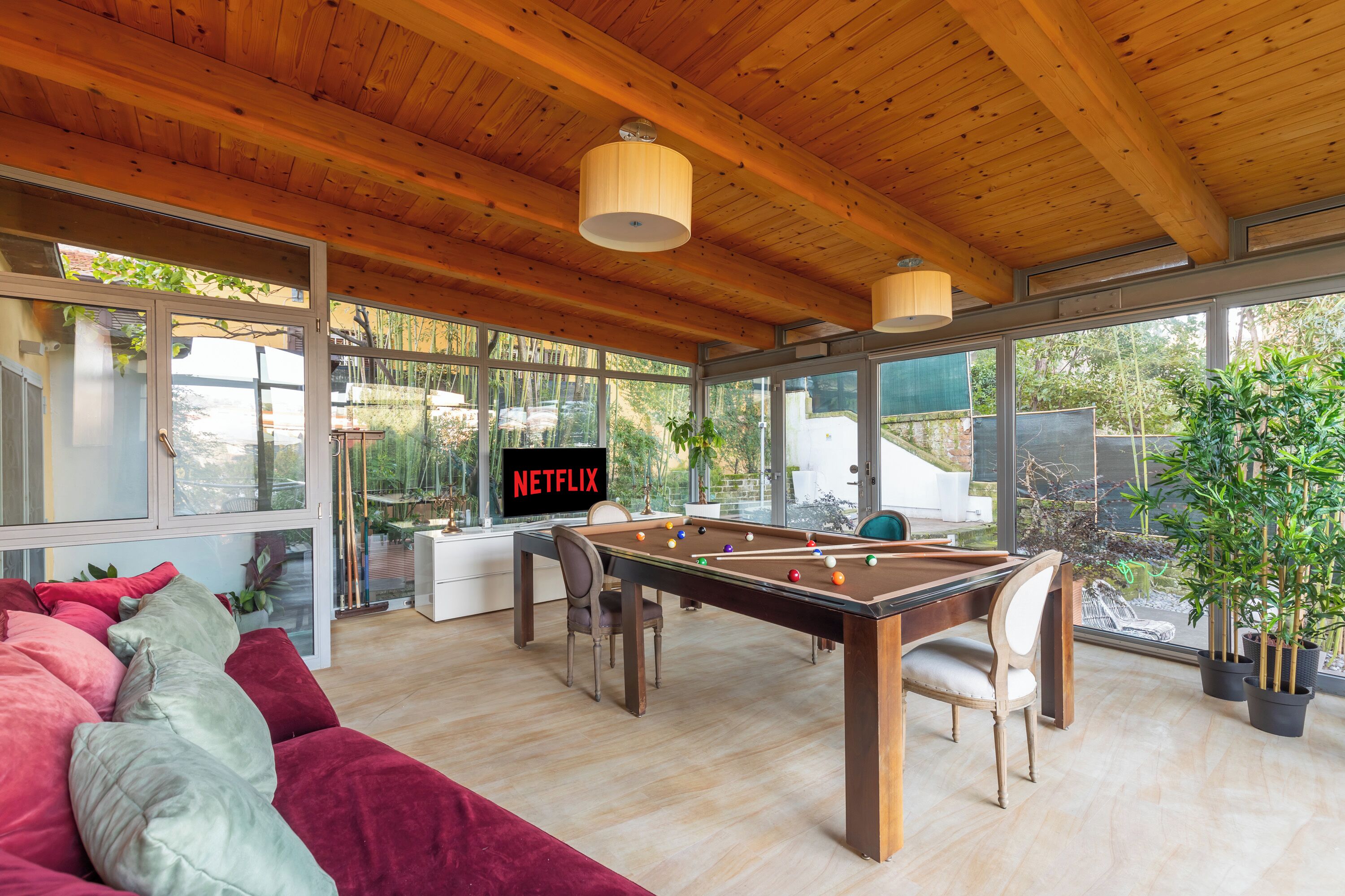 A spacious room with a pool table, comfortable seating, and large windows offering a view of the outdoors.