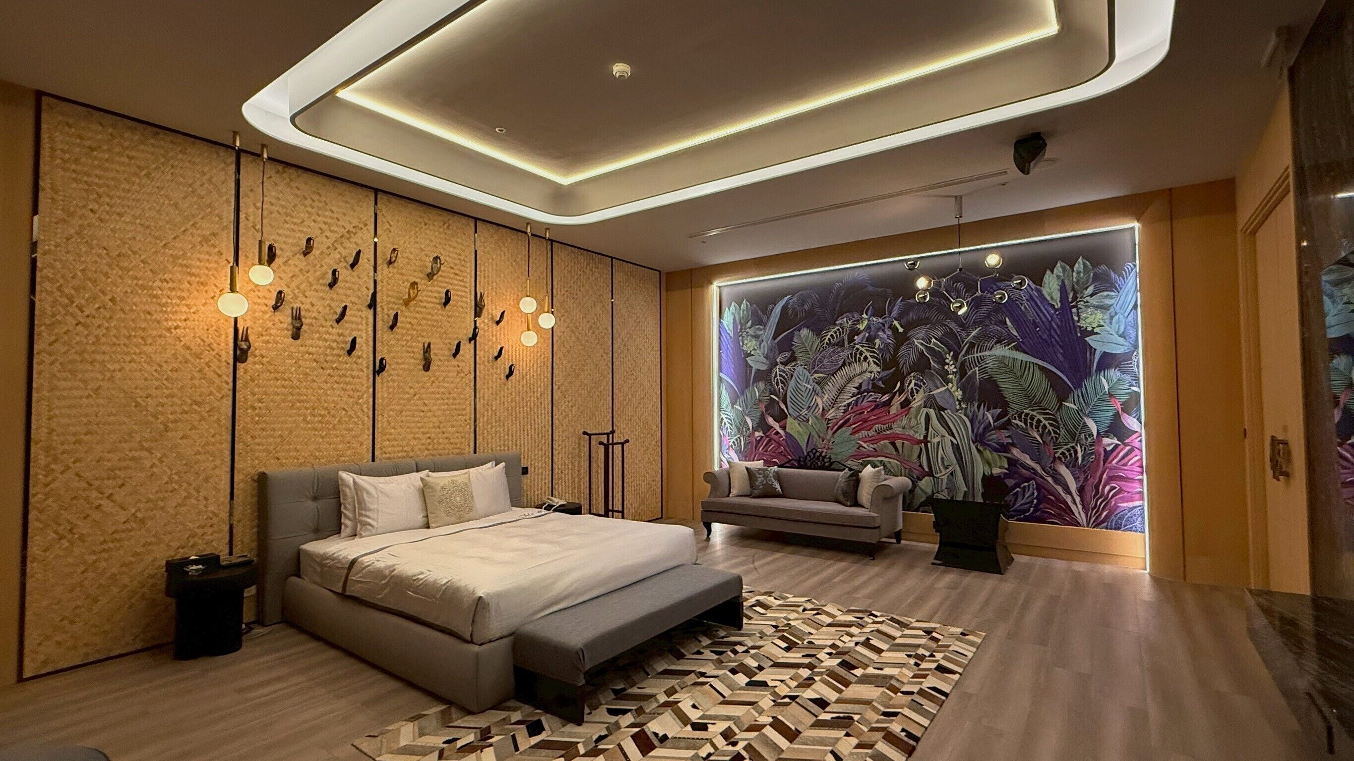 A modern bedroom with a large bed, a sofa, a patterned rug, and a wall mural.