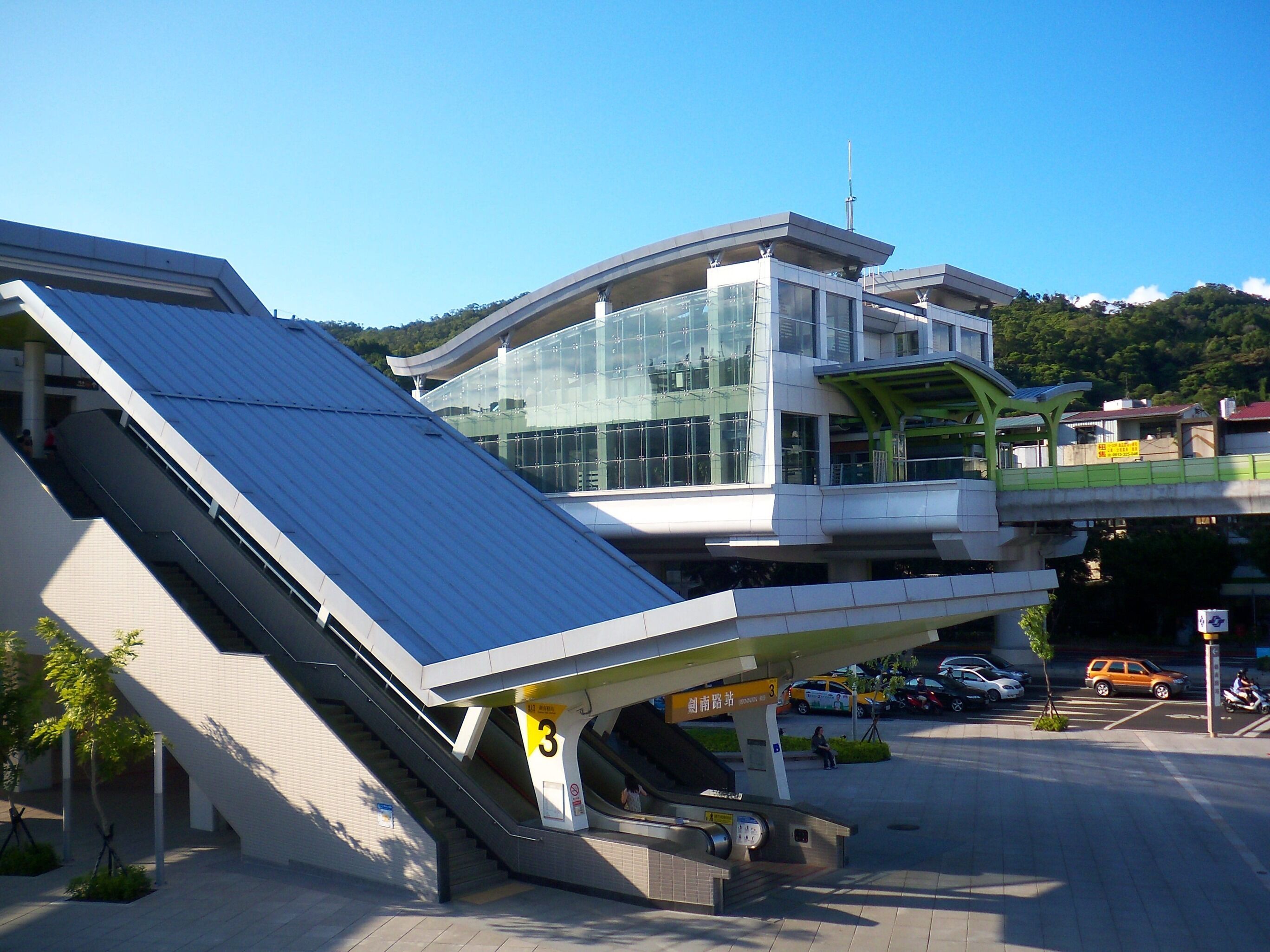A modern building with a glass facade, a green overpass, and a staircase leading to an upper level.
