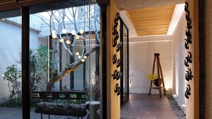 Een modern interieur met een glazen deur naar een tuin, een houten bankje en een ladder tegen een structuurwand.