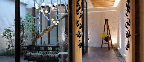 A modern interior with a glass door leading to a garden, a wooden bench, and a ladder against a textured wall.