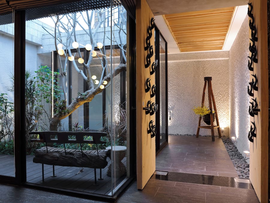 A modern interior with a glass door leading to a garden, a wooden bench, and a ladder against a textured wall.
