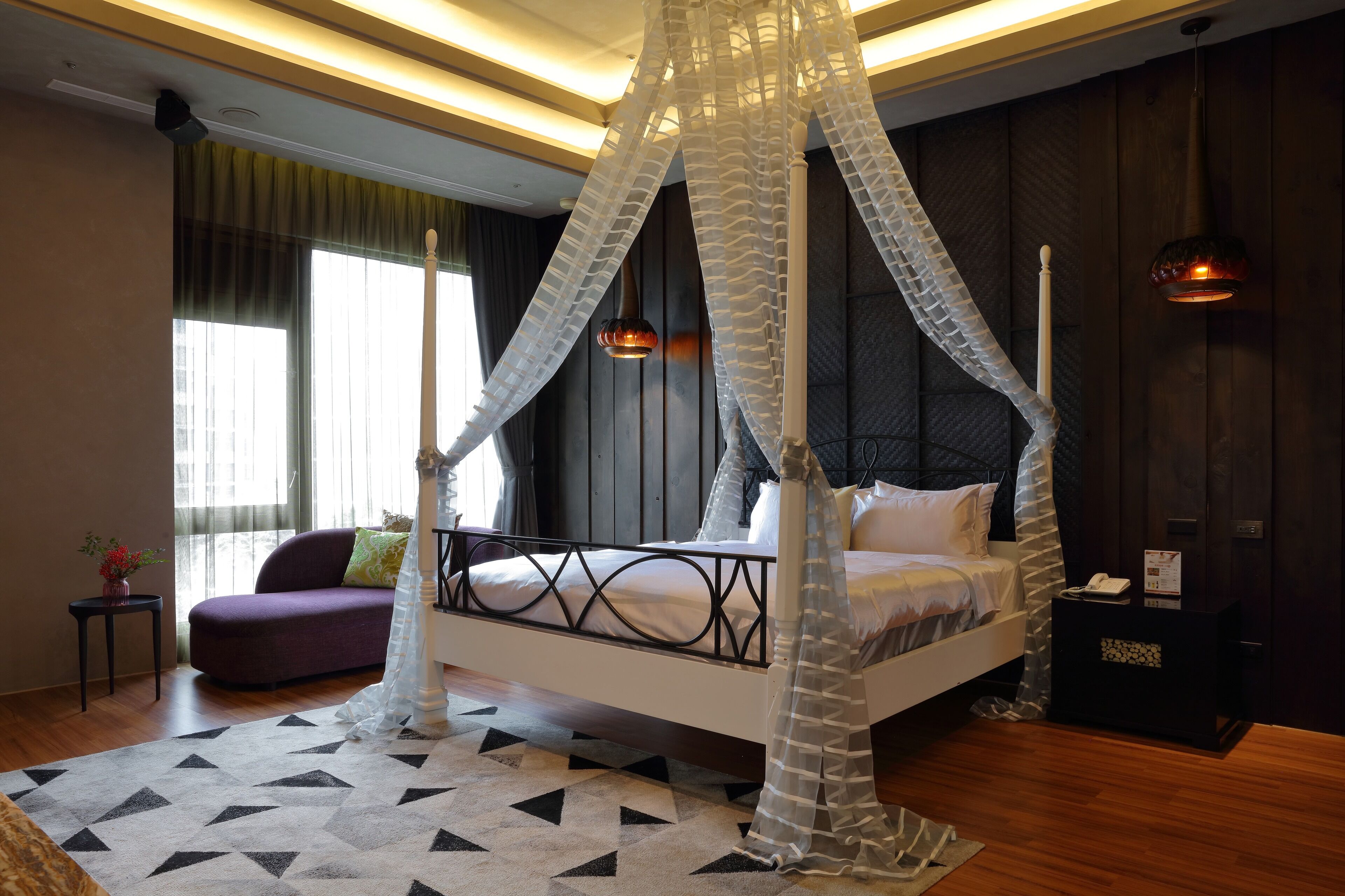 Une chambre à coucher moderne avec un lit à baldaquin, un canapé, une petite table d’appoint et une table de chevet.