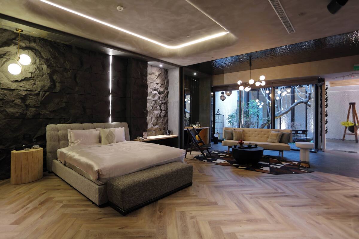 A modern bedroom with a large bed, a wooden floor, a stone accent wall, and a seating area with a sofa and coffee table.