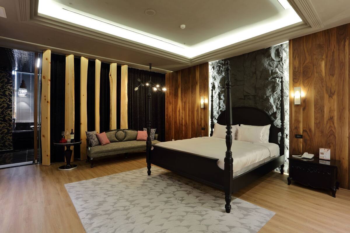 A bedroom with a four-poster bed, a sofa, and a stone accent wall.