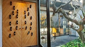 Een houten wand met handgemaakte uitsnijdingen, een glazen deur en uitzicht op een terras met planten en een boom.