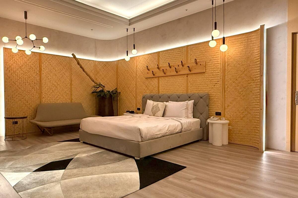 A modern bedroom with a large bed, a sofa, a small table, and a plant.