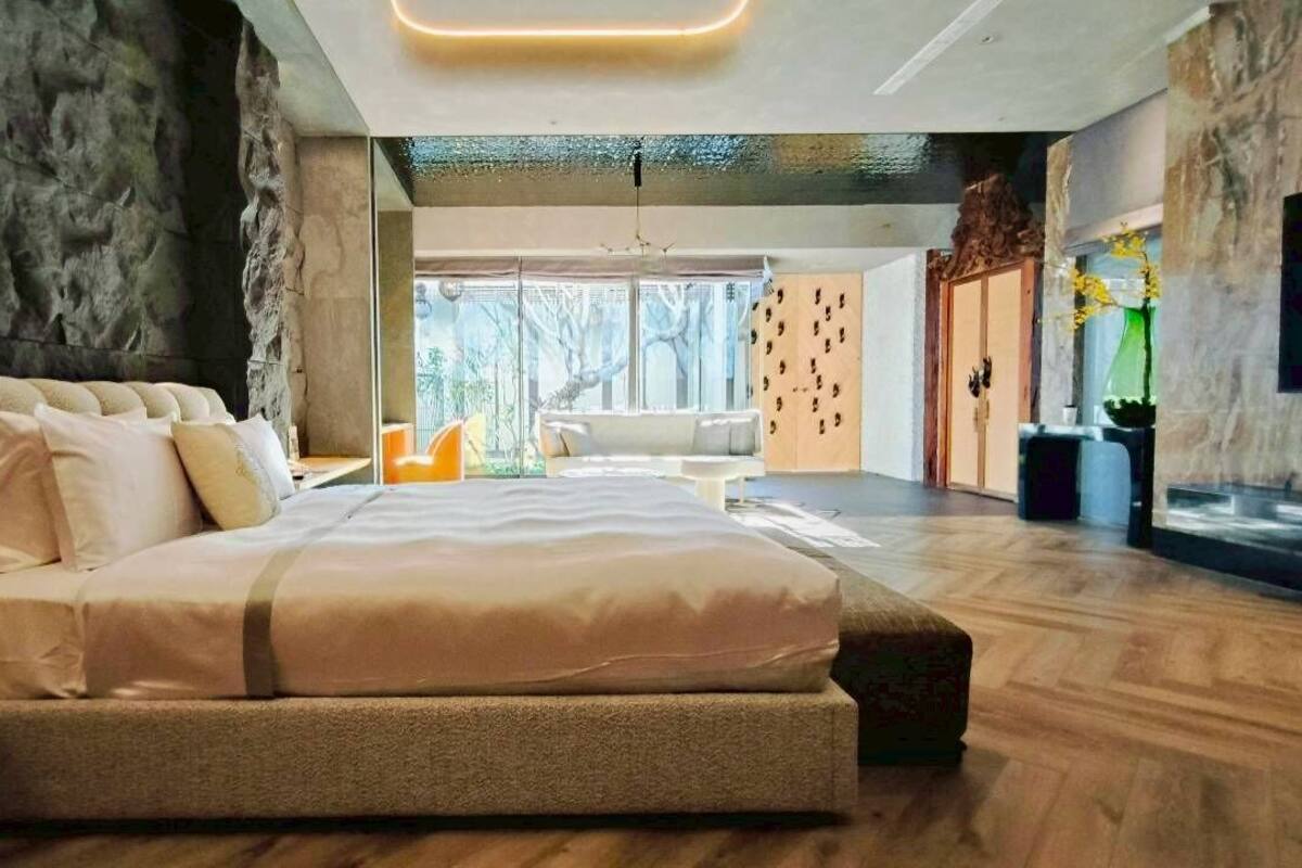 A modern bedroom with a large bed, a stone wall, and a view of the outdoors.