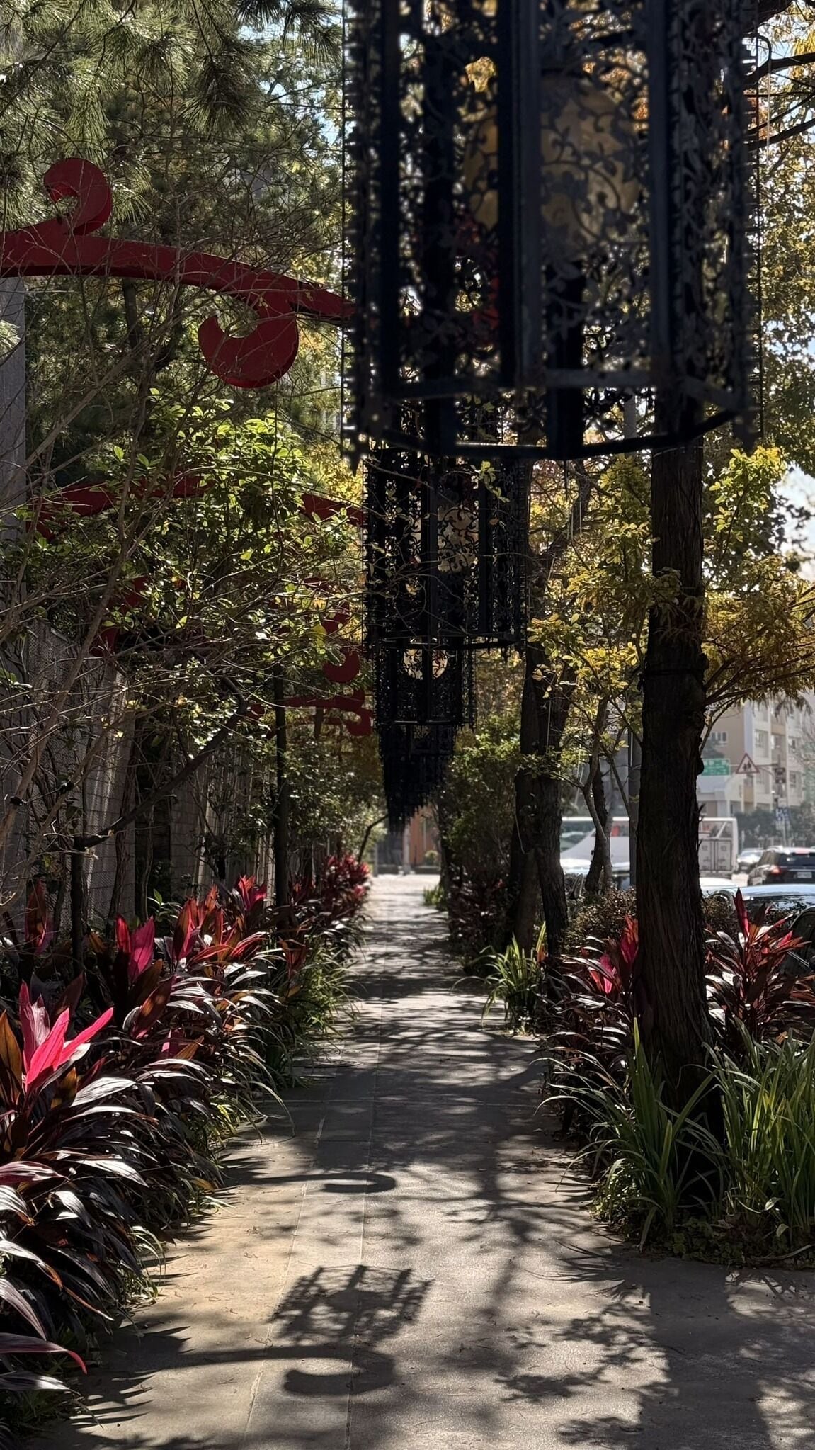 A pathway lined with trees and plants, leading to a building with a metal gate.