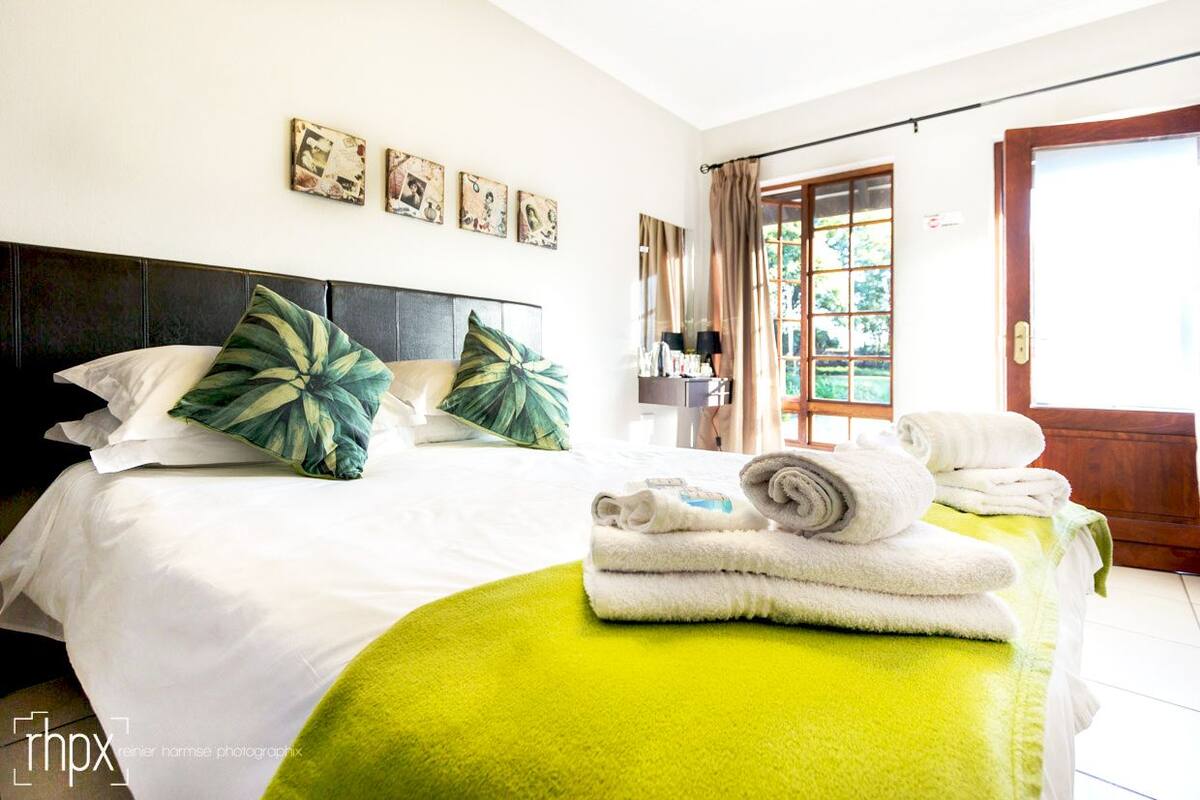 Een hotelkamer met een bed, een groen vloerkleed en een stap handdoeken op het bed.