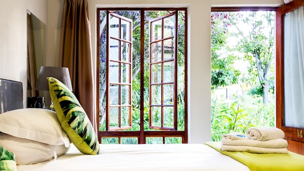 Een hotelkamer met een bed, kussens, een lamp en uitzicht op groen door een raam.