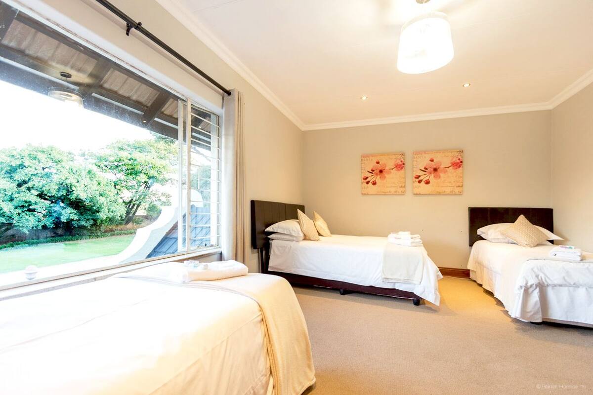 Een hotelkamer met twee bedden, een groot raam met uitzicht op groen en een plafondlamp.