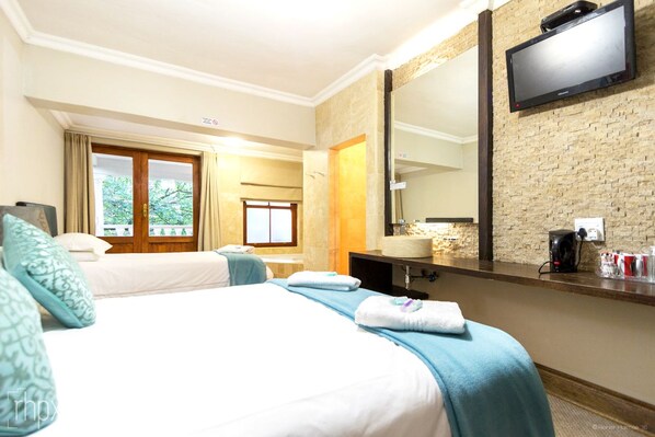 A hotel room with two beds, a large mirror, a television, and a bathroom visible through an open door.