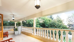 Een overdekt terras met een witte balustrade, plantenbakken en houten banken.