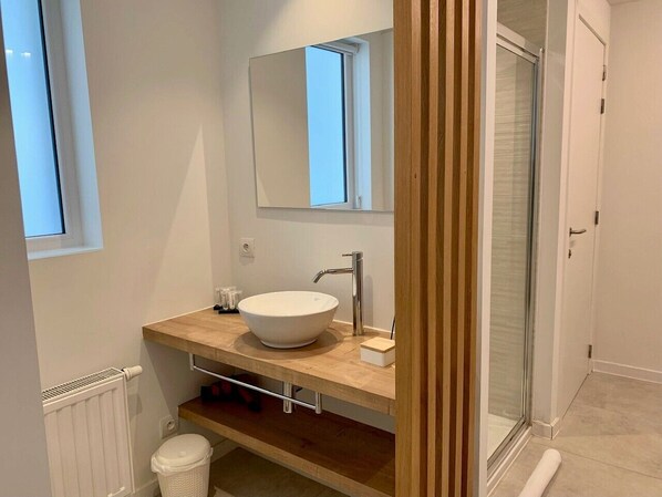 Un baño moderno con un lavamanos grande blanco, un espejo y una ducha.