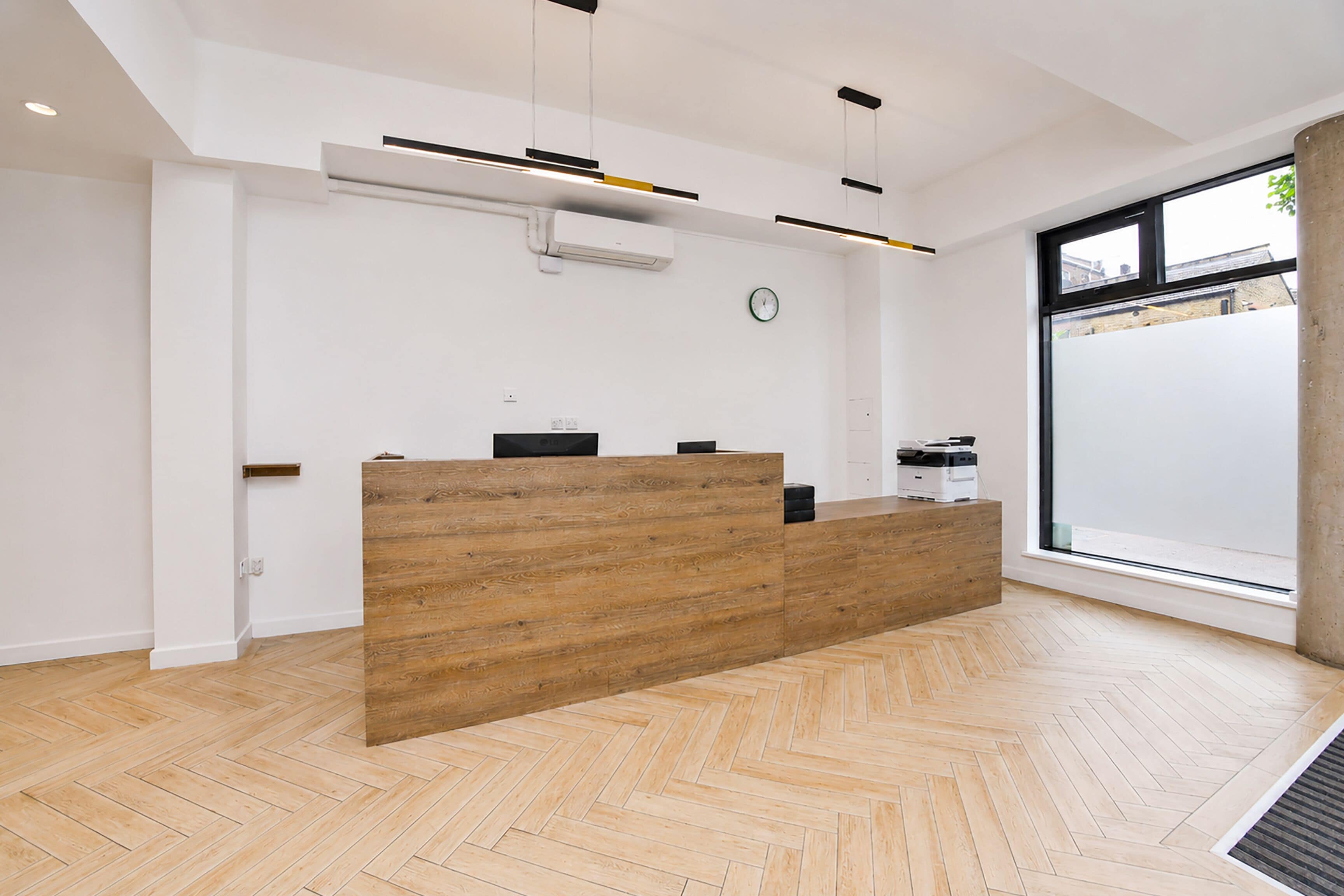 Ein Empfangsbereich mit einem Holzbüro, einer Wanduhr und einem großen Fenster.