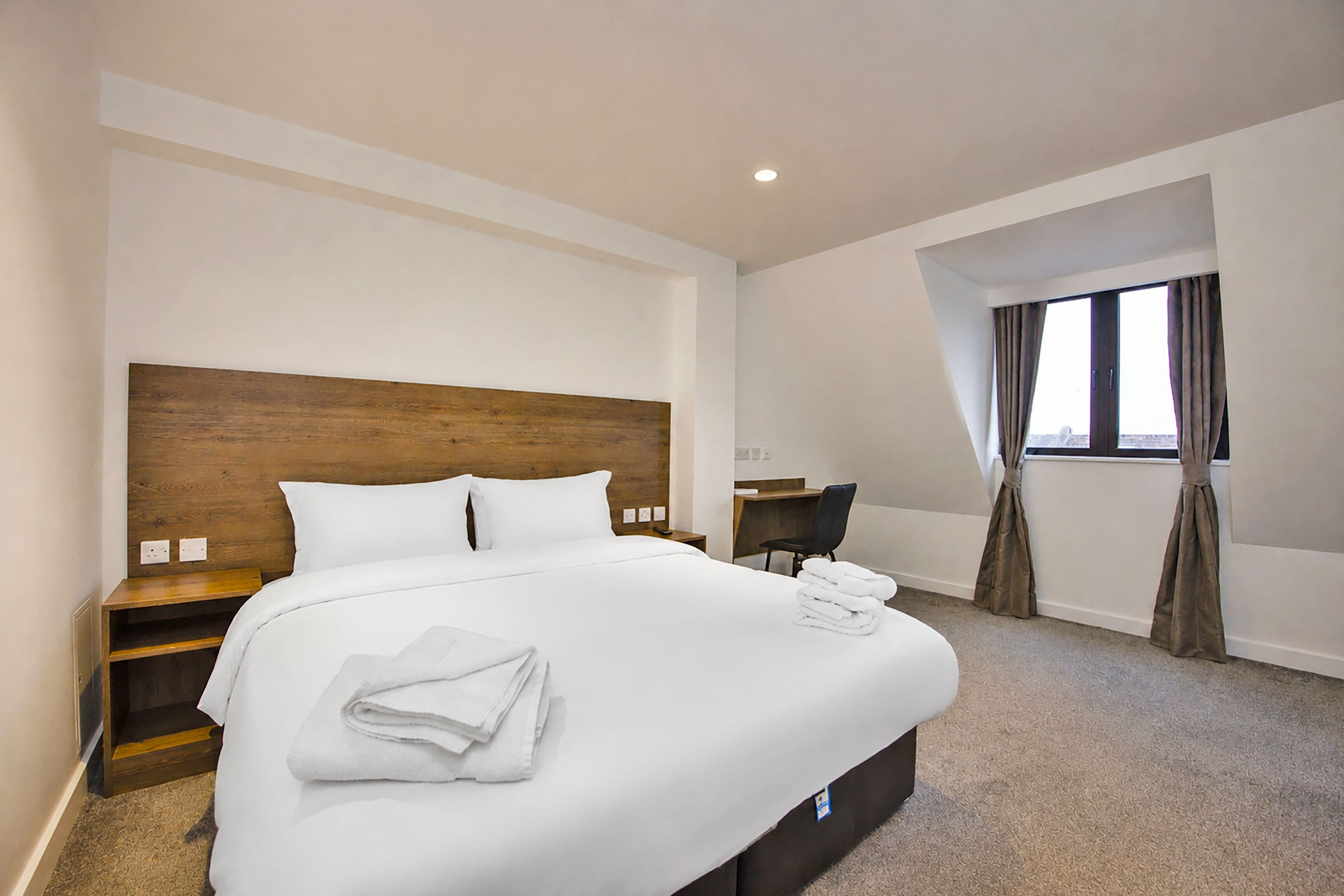 A hotel room with a large bed, a desk, a chair, and a window with curtains.