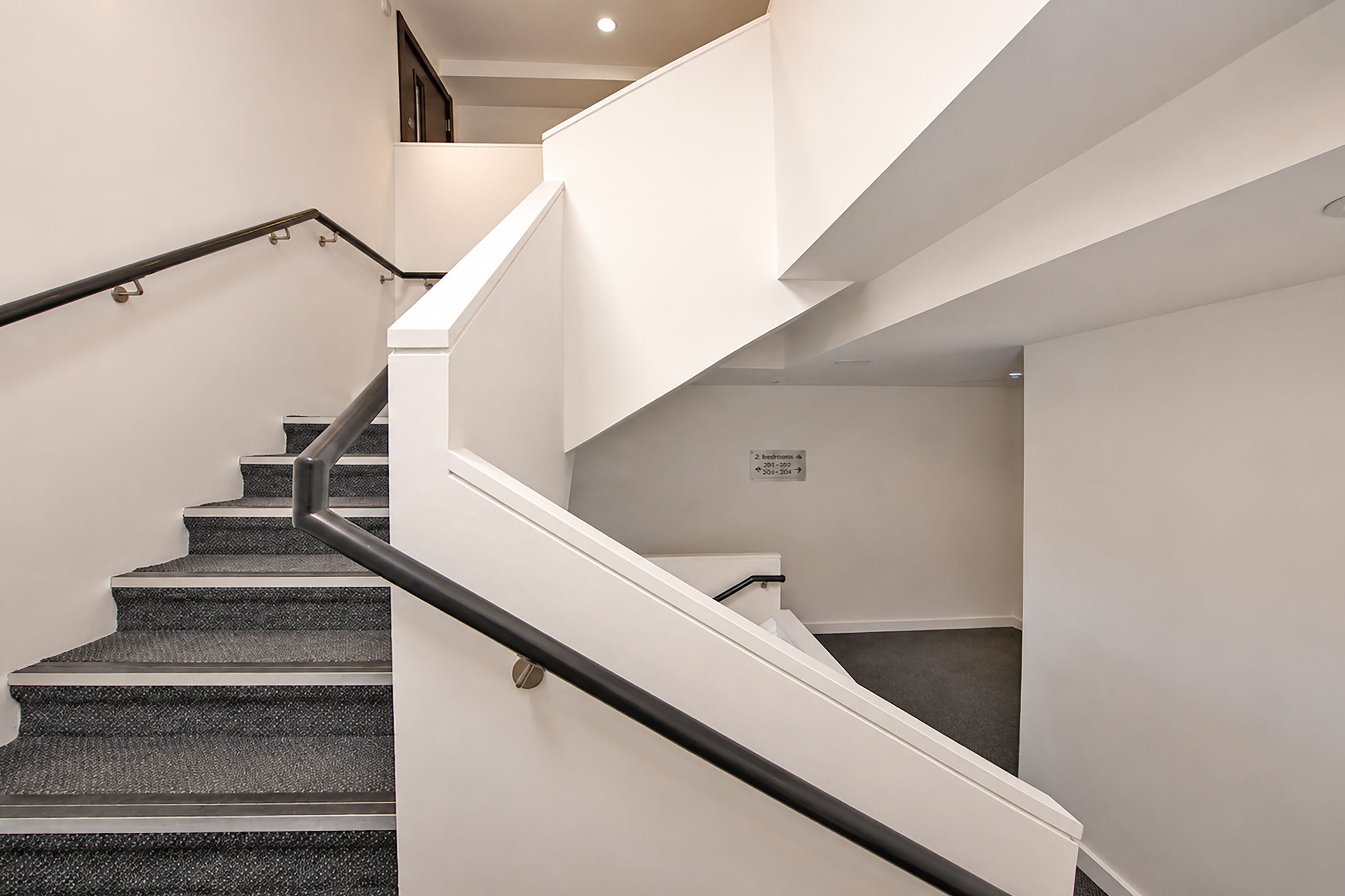 Una escalera con barandilla, peldaños alfombrados y un letrero que indica 2 habitaciones.