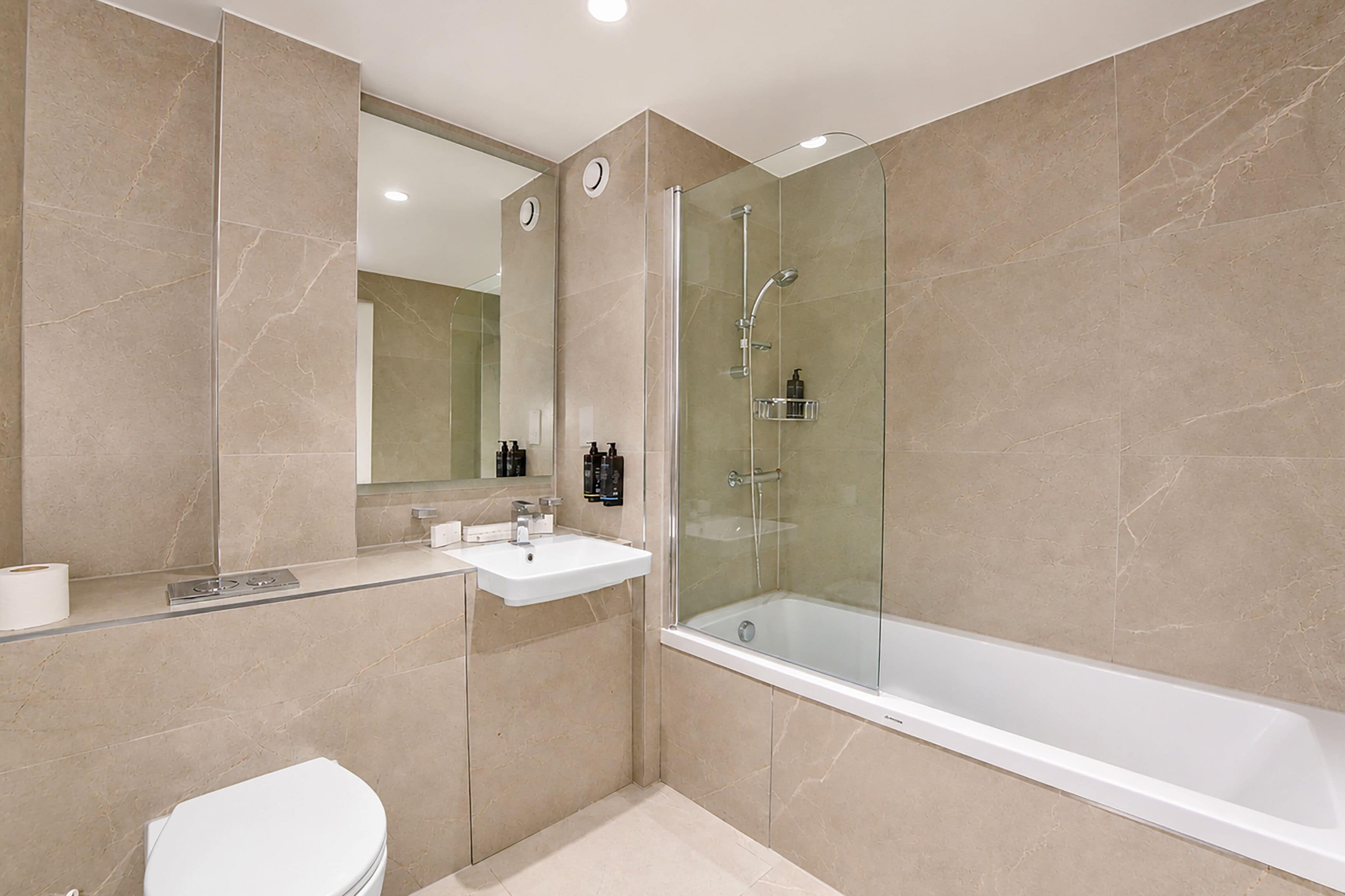 Un baño moderno con ducha envuelta en vidrio, un lavamanos blanco y un inodoro.