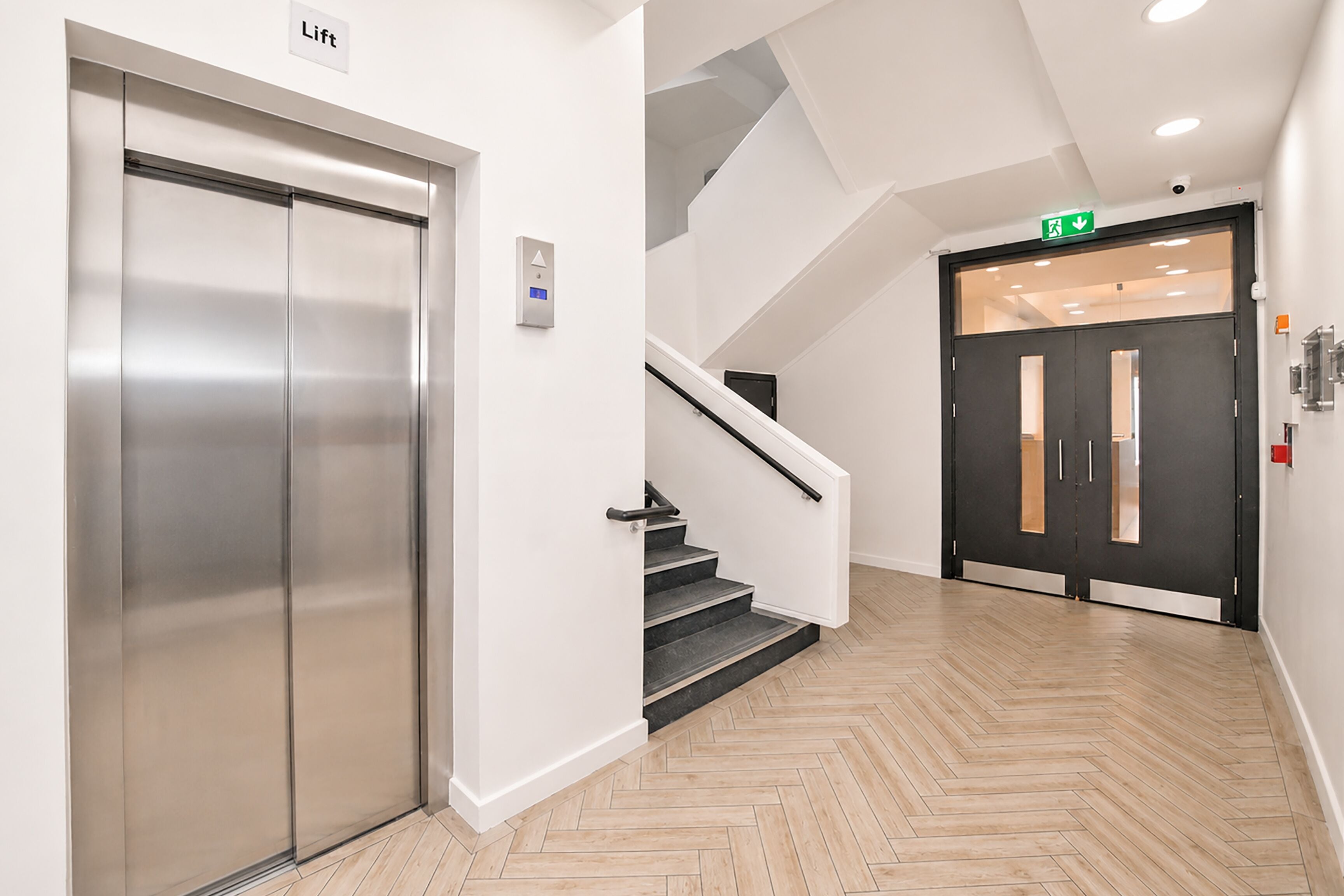 A modern elevator, a staircase, and a door with an emergency exit sign.
