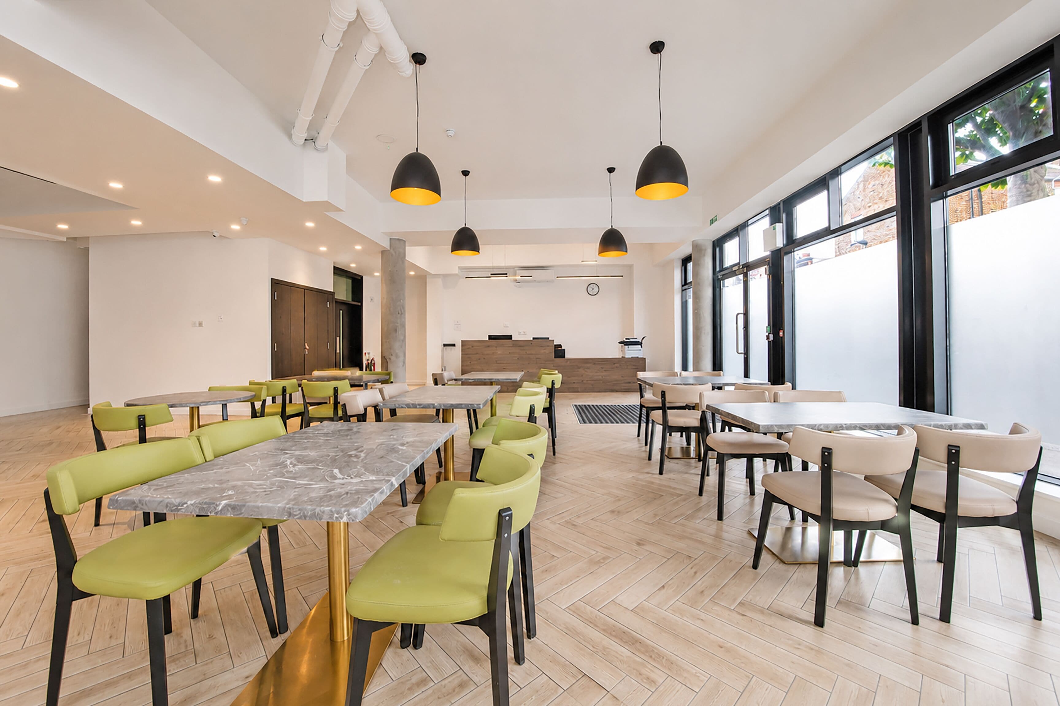Un vaste espace de restauration avec de nombreuses tables et chaises, une grande fenêtre laissant entrer la lumière naturelle et un comptoir central.