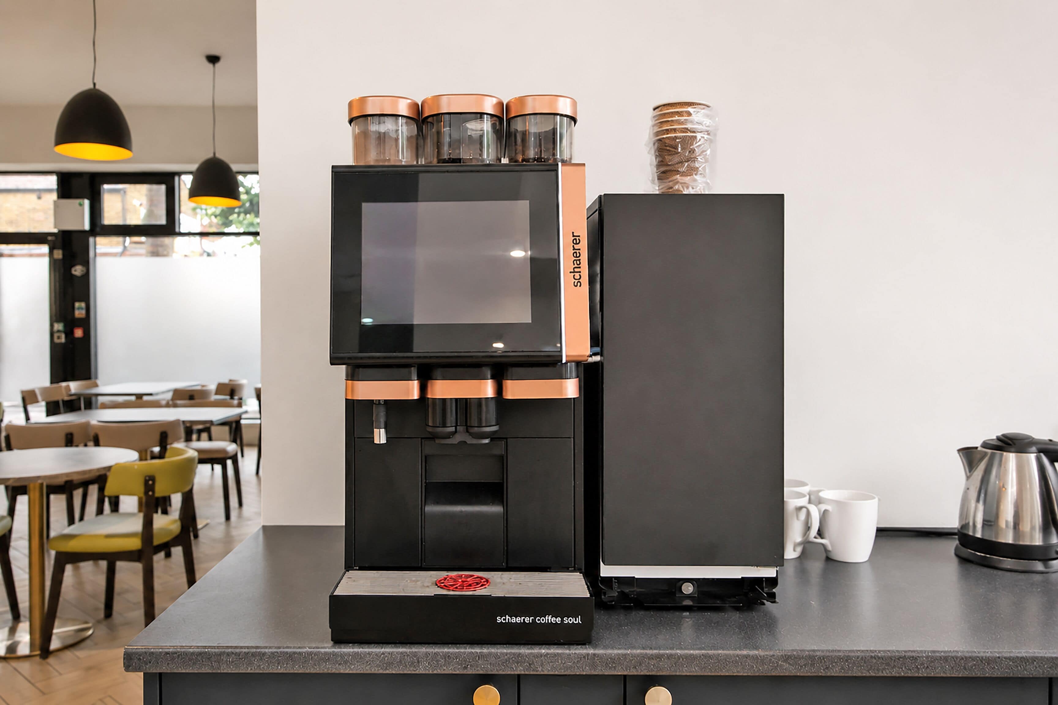 A coffee machine with a digital display, a coffee grinder, and a kettle on a counter.