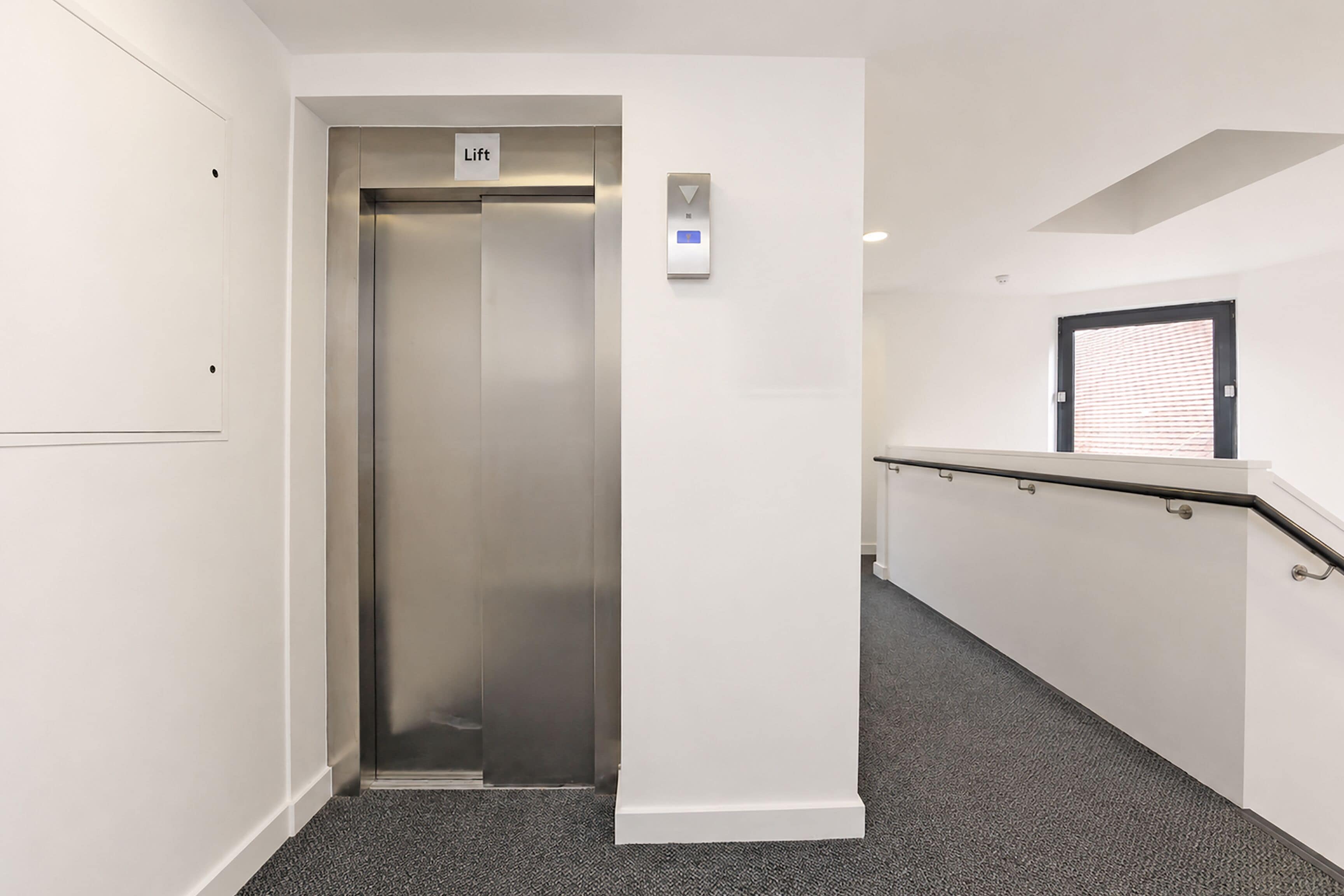 A hallway with a lift, a door with a window, and a handrail.