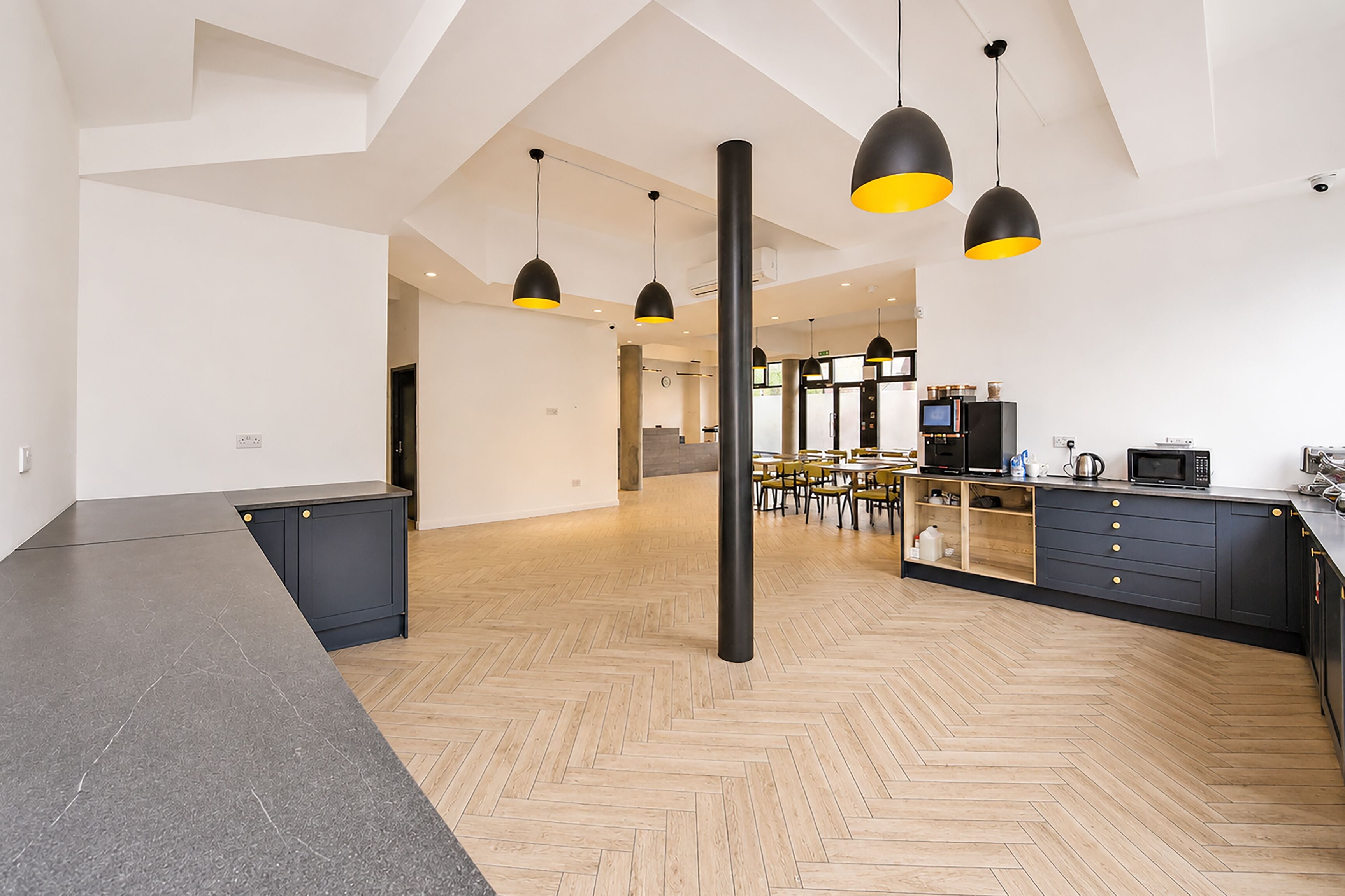 Una cocina amplia con electrodomésticos modernos, un comedor con sillas amarillas y un suelo de madera en espiga.
