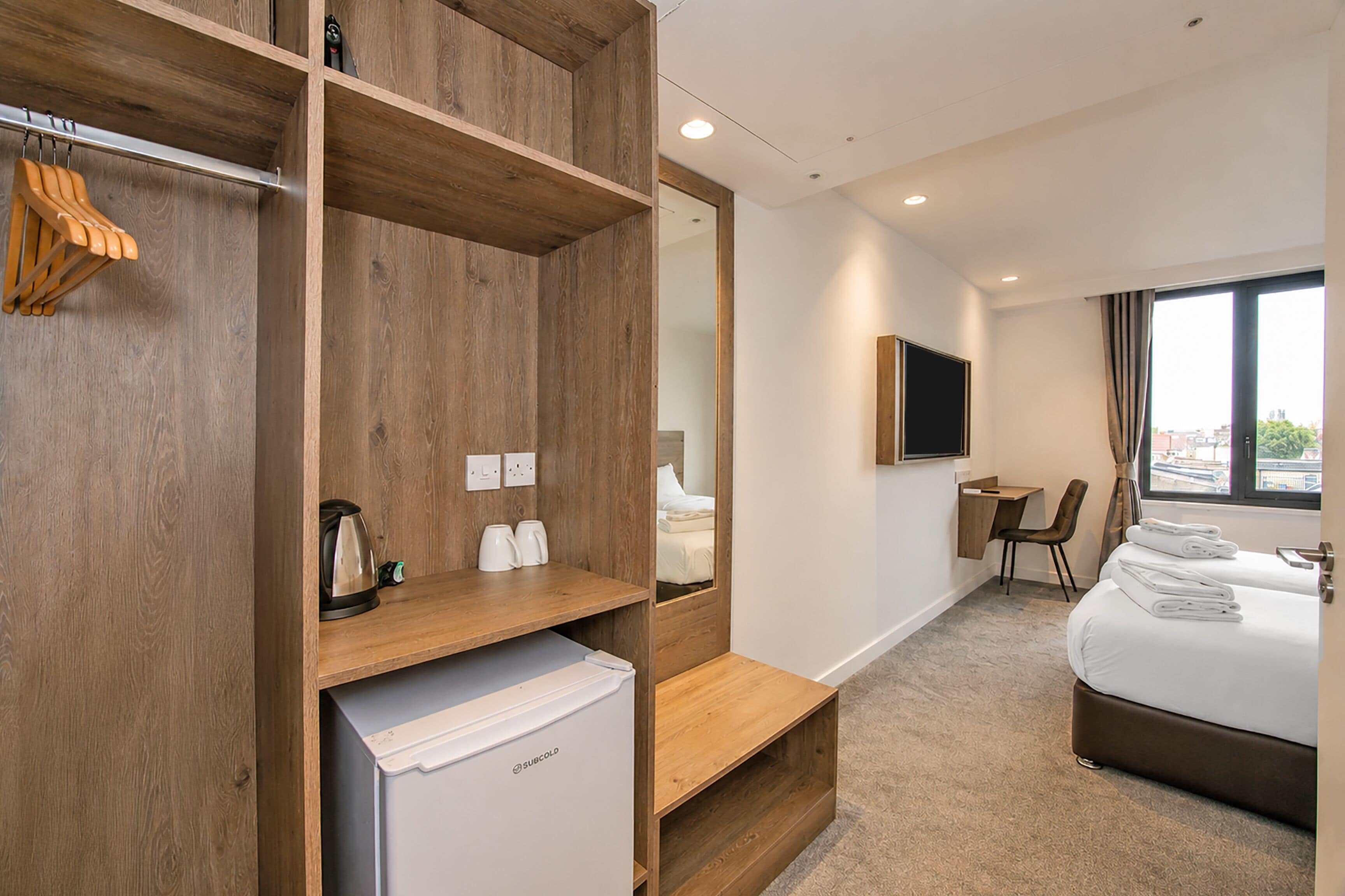Ein Hotelzimmer mit Bett, Schreibtisch, Stuhl, Kleiderschrank und kleinem Kühlschrank.