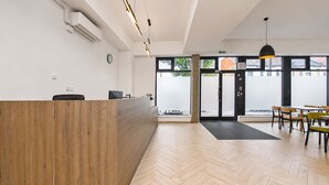 Zona de recepción con mostrador de madera, una computadora, un reloj y un amplio ventanal con vistas al exterior.